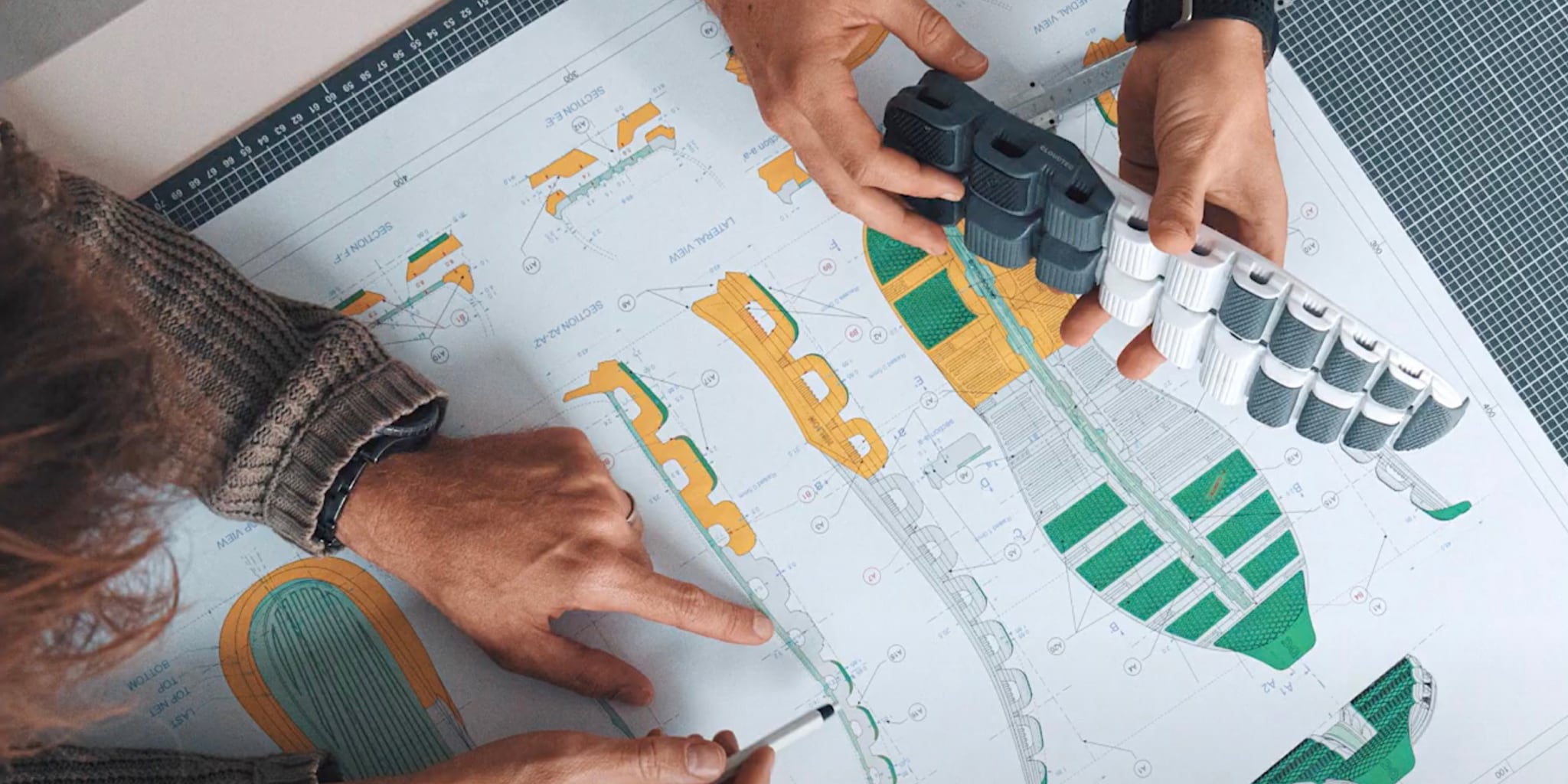 Two people working on a design project with stencils and markers on a large sheet of paper - Cloudtec