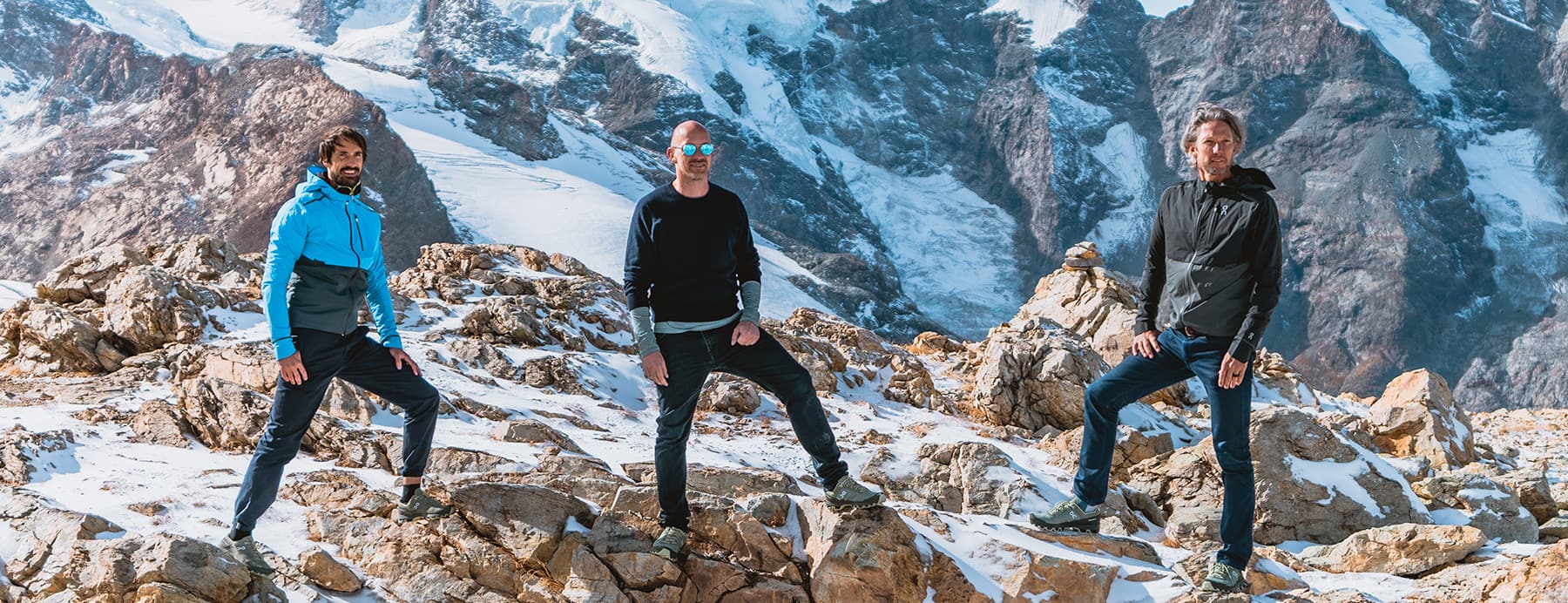 On founders standing on a rocky mountain peak with snow-covered mountains in the background