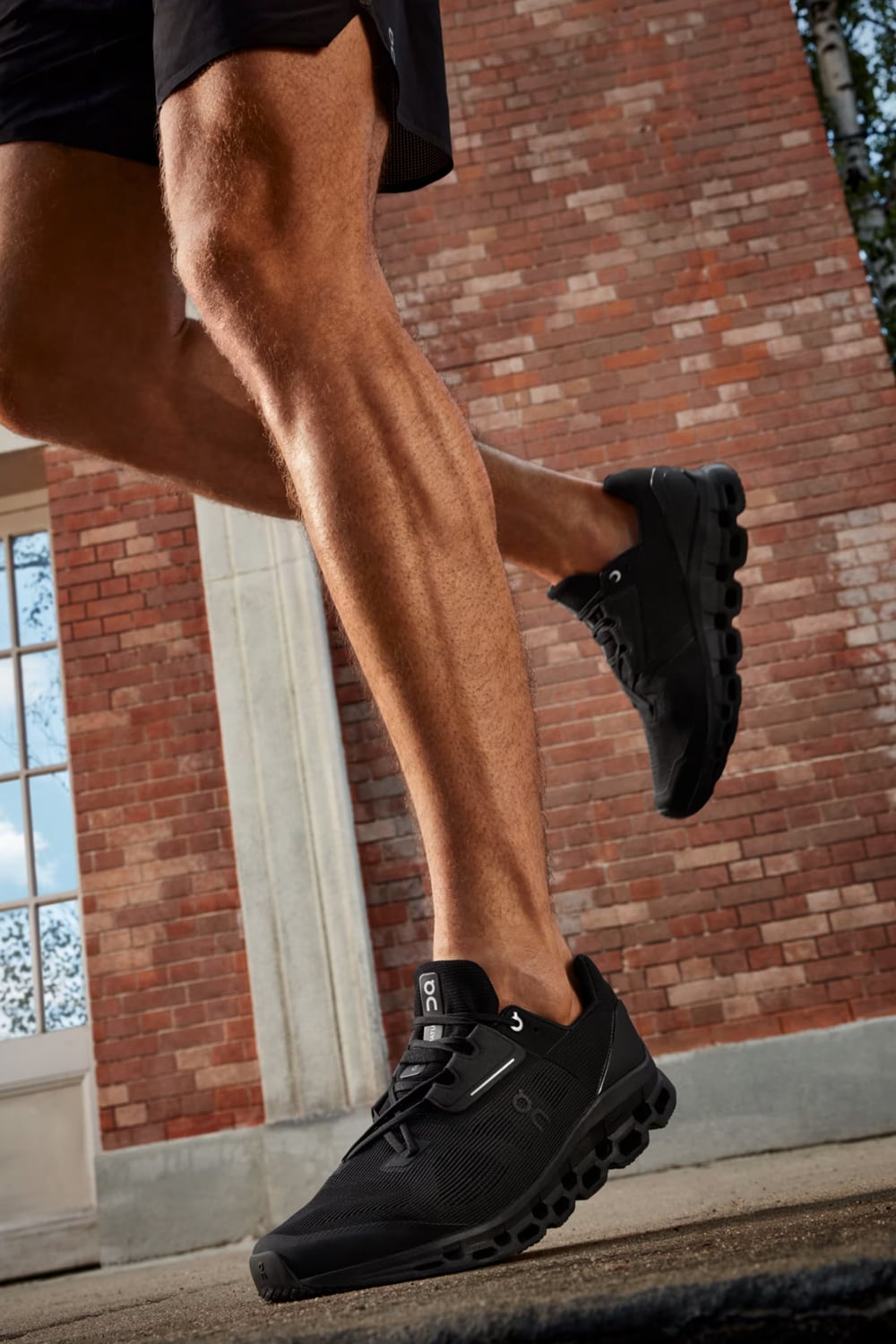 Person wearing black Cloudstratus 3 shoes with a brick building in the background