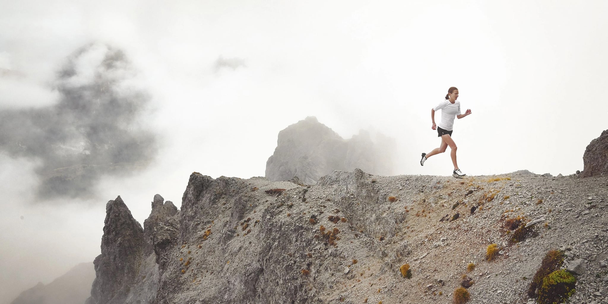 Person running on a rocky mountain peak with misty background