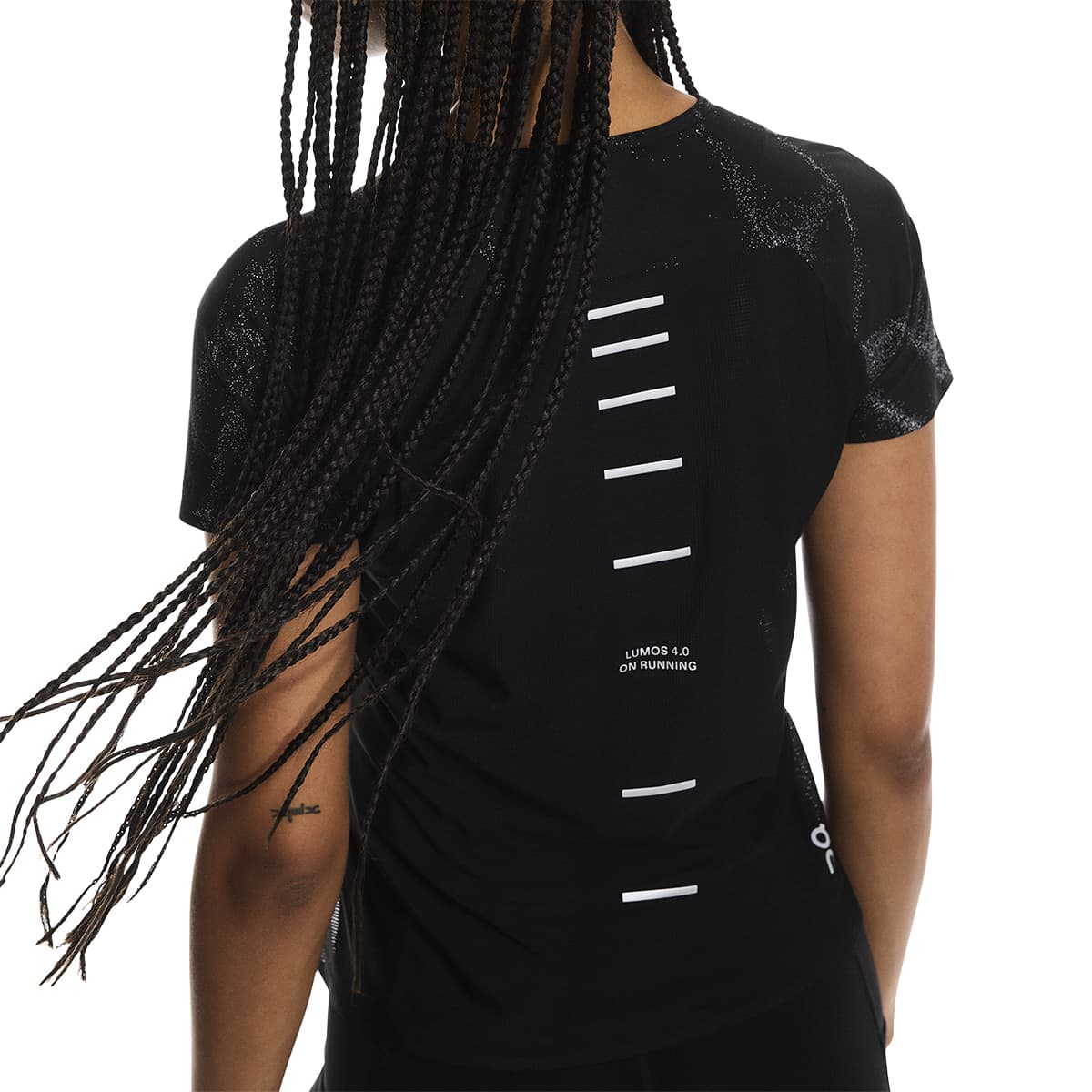 Female model wearing the On Apparel - Performance T Lumos Colour Black, with reflective bars visible