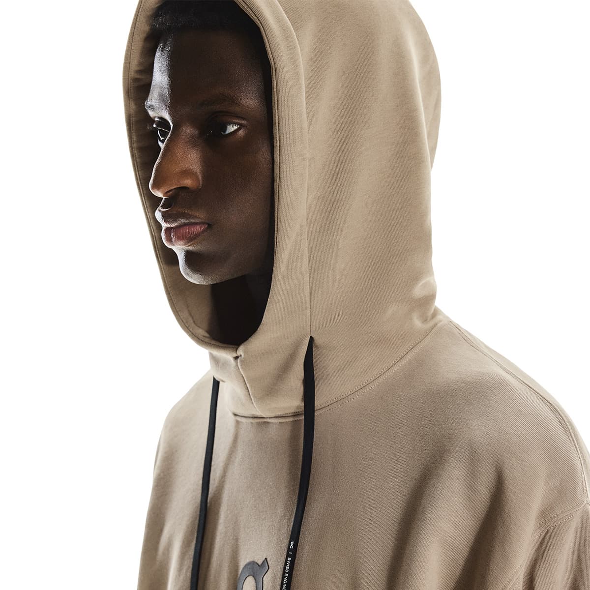 Close-up side profile of male model wearing the hood up on the On Club Hoodie in Desert