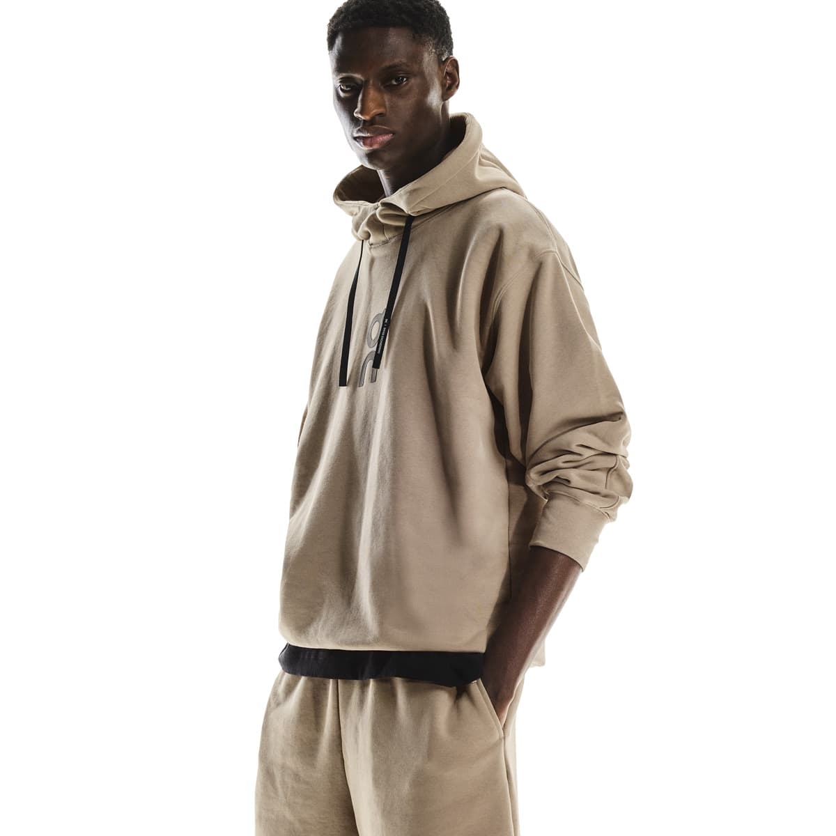 Angled front view of male model with sleeves scrunched, wearing the On Club Hoodie in Desert