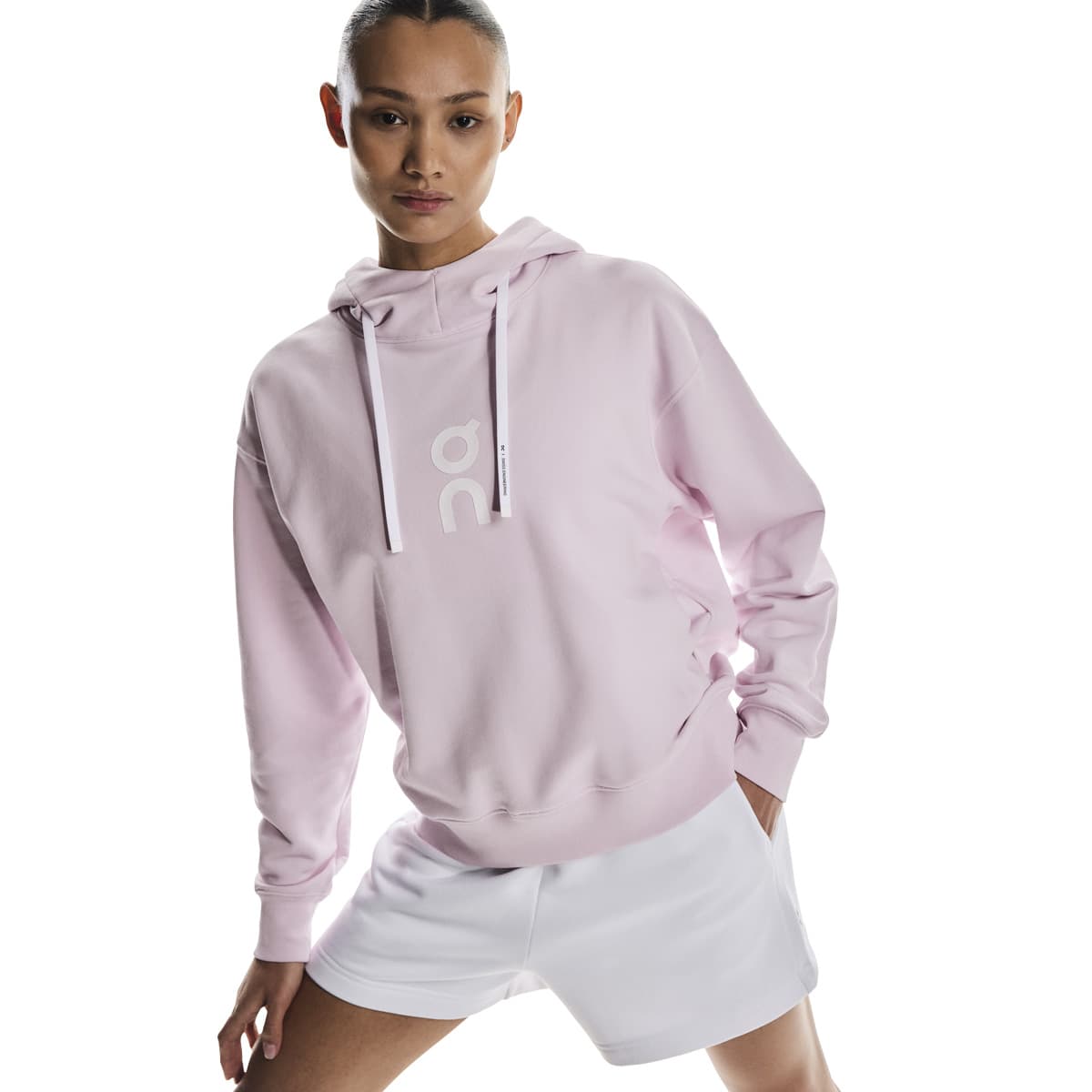 Angled front pose of female model in the On Club Hoodie in Orchid with hands in pockets