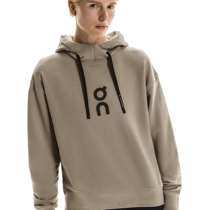 Close-up of female model in the On Club Hoodie in Desert showing logo and hood detail 